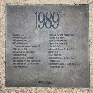 A metal plaque titled '1989' listing various software releases including SQL Server 1.0, QuickC 2.0, and Microsoft Excel 2.2, among others, highlighting key technological advancements from that year.